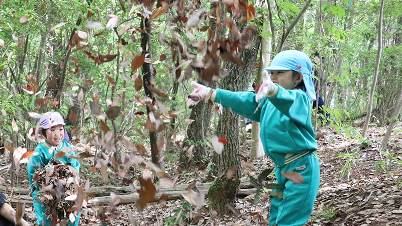 落ち葉の中で遊ぶこどもたちと学生