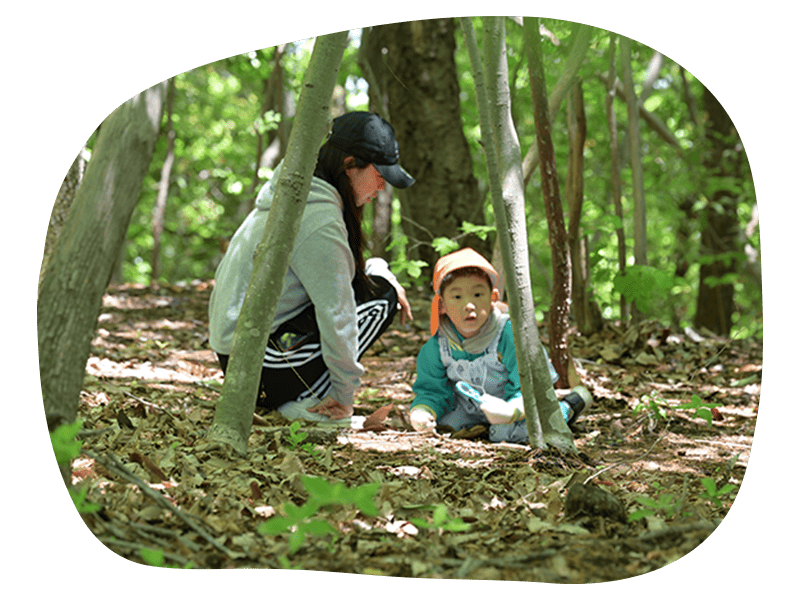 森の中で学生とこどもが何かをさがしている